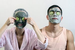 A woman and a man wearing facial masks along with cucumbers over their eyes