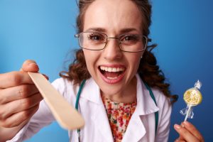 A doctor holding a tongue depressor and a lollipop 