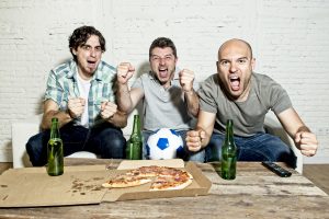 Three men sitting on the couch and screaming while watching the game