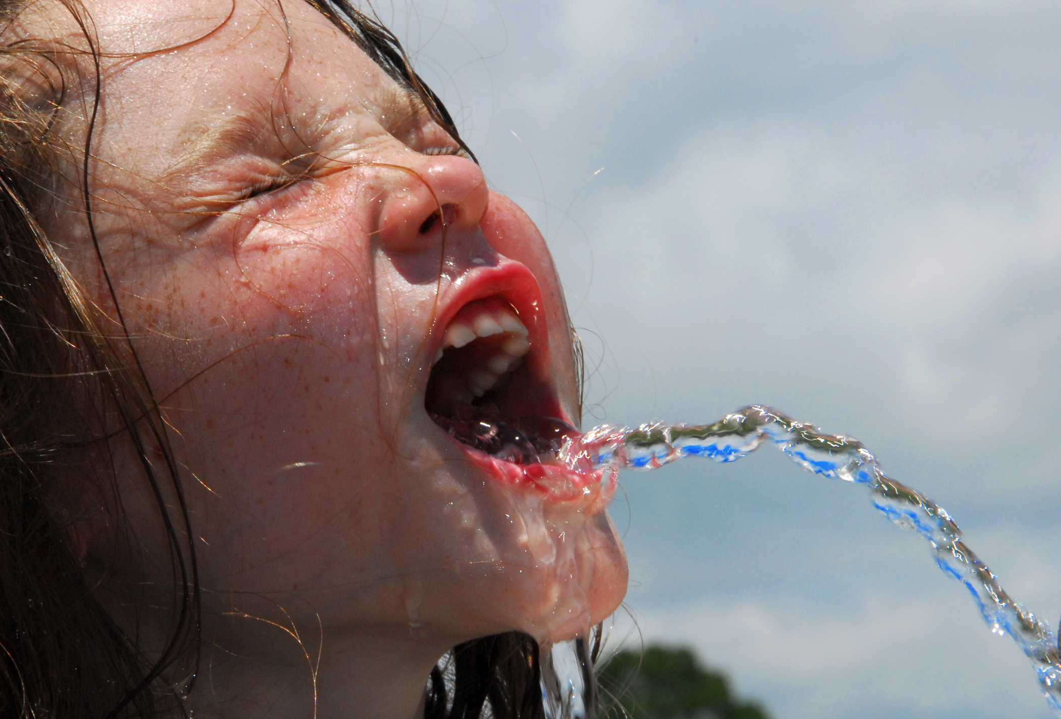 Little girl with eyes closed and a stream of water if coming out of her mouth