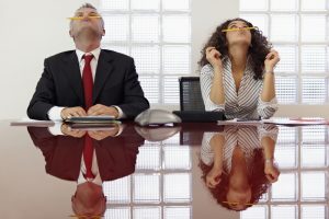 Two business people at a meeting, with bored expressions, while balancing pencils on their noses