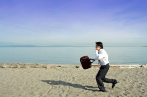 Businessman holding a briefcase while speaking on the phone and running on the beach