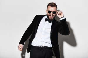 Man in tuxedo striking a pose with his sunglasses 