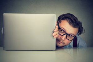 Businessman with a tired face peeking out from the side of his computer