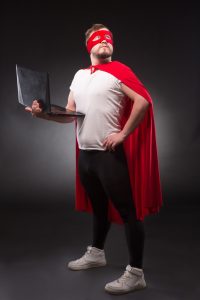 Man dressed as a superhero in the superhero pose while holding a computer