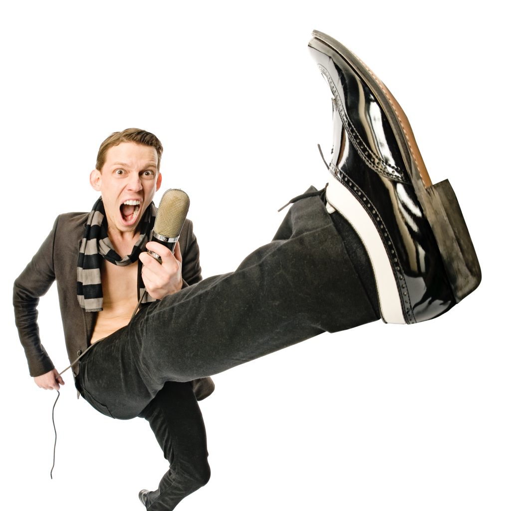 Performer singing into microphone while kicking leg up into the air