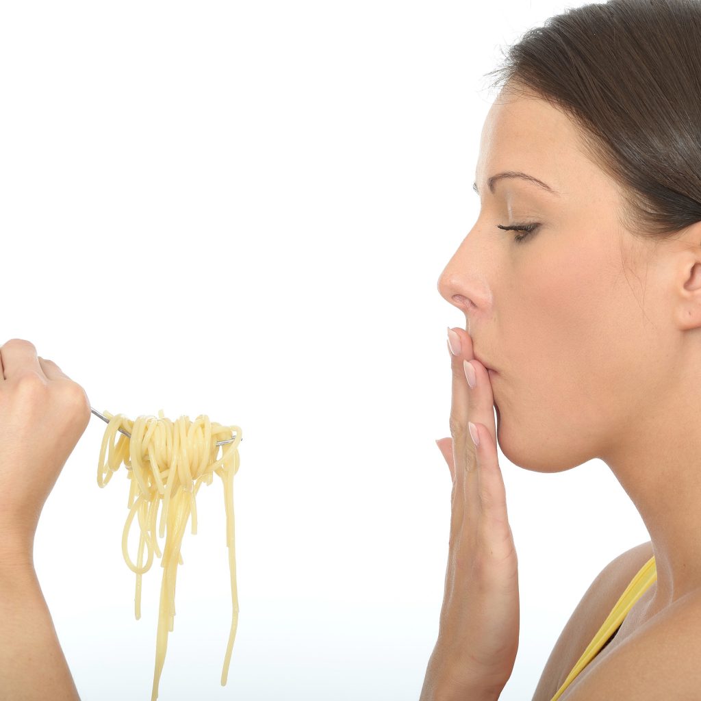 Woman covering mouth with nauseous expression while looking at a fork full of pasta