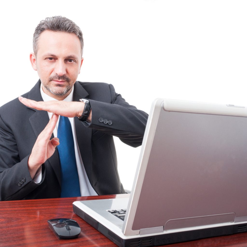 Businessman holding up the time out sign while in front of his computer