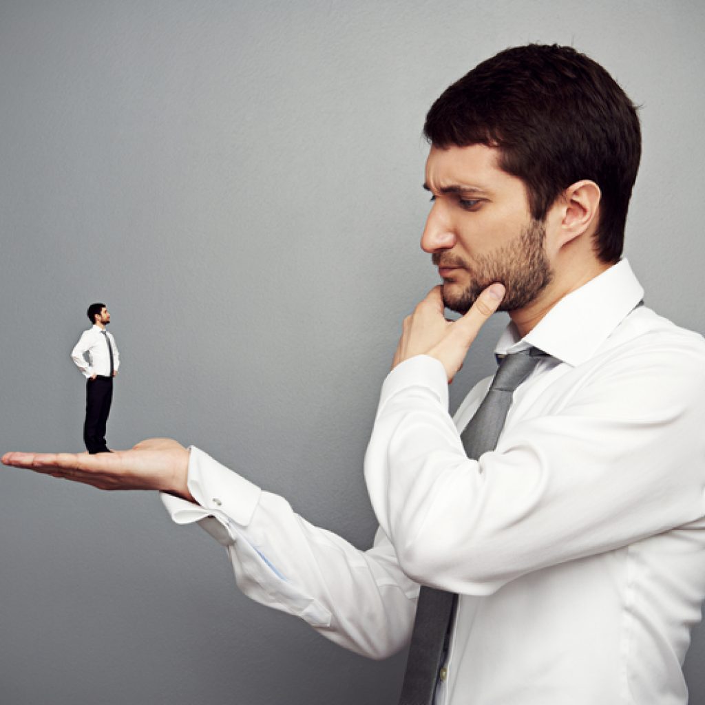 Businessman pondering while he holds a smaller version business man in his hand