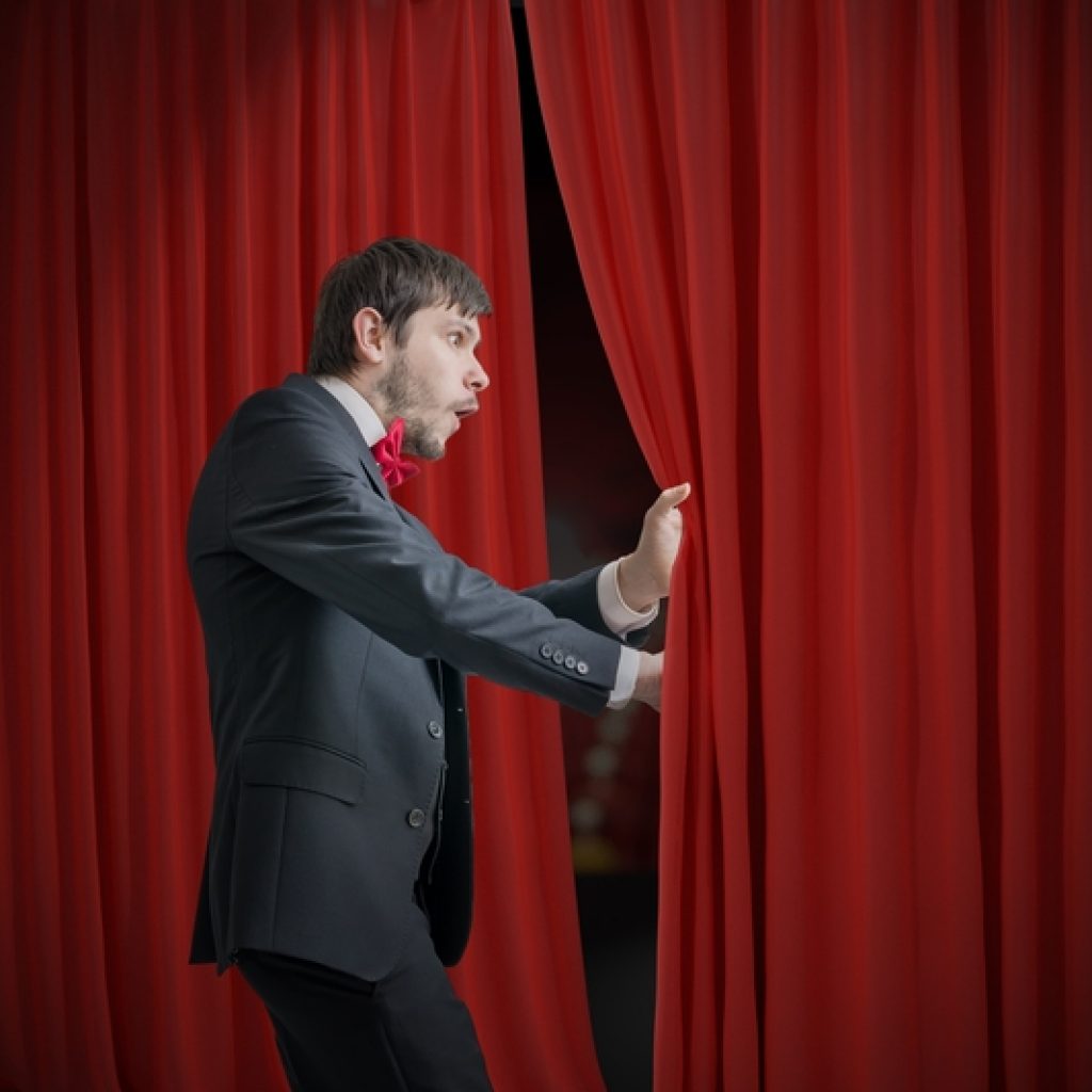 Man getting ready to go on stage, but getting scared when peeking through the curtain at the audience